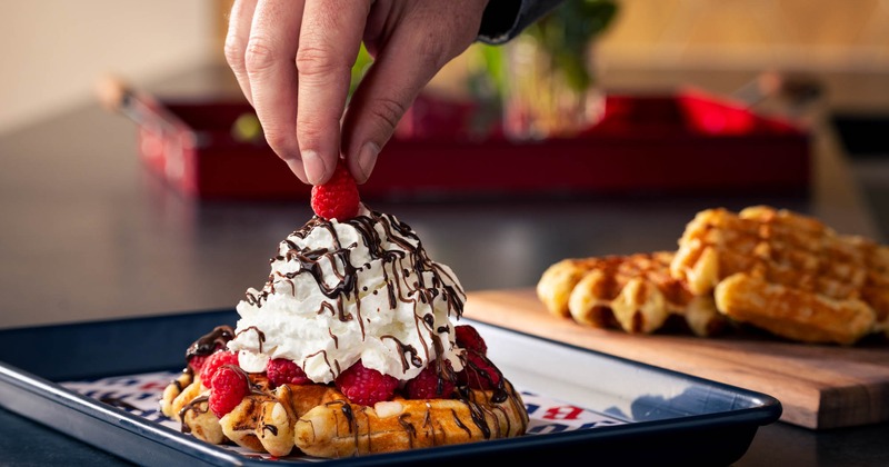 Sweet waffle topped with fresh raspberries, whipped cream and chocolate drizzle