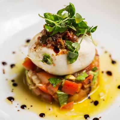 Burrata cheese served over a tower of avocado, heirloom tomatoes, red onions, and olive tapenade.