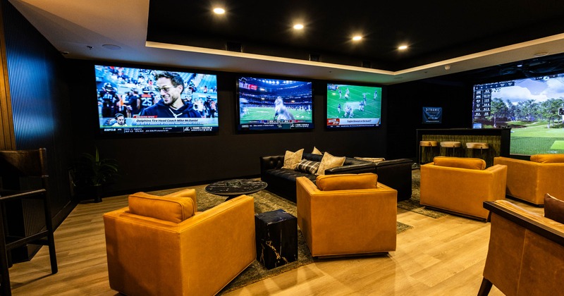 Interior seating area with multiple TVs, armchairs, a couch, and a bar area