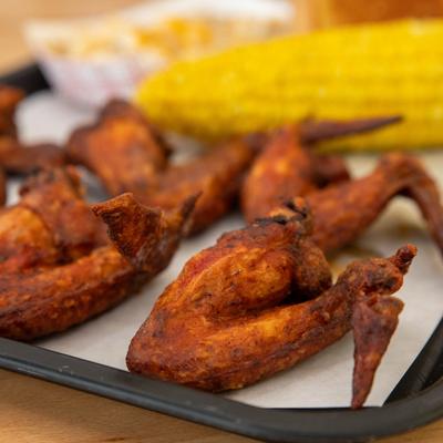 Close up of hot wings on a plate, a corn on the cob is visible.