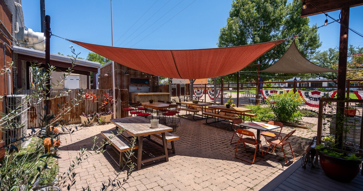 Outdoor patio with wooden tables and chairs on a brick floor