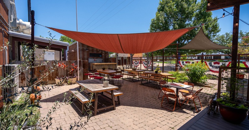 Outdoor patio with wooden tables and chairs on a brick floor