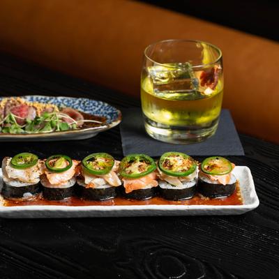 Plate of sushi rolls topped with jalapeno peppers served with a drink.