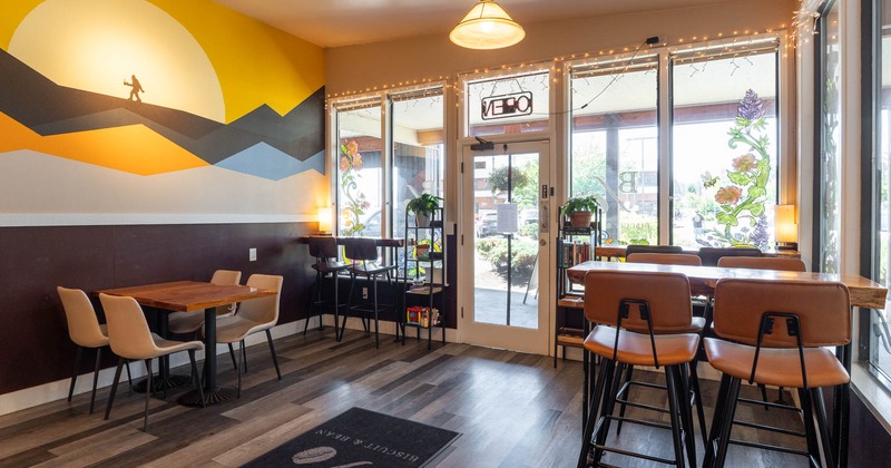 Café interior with a mural of mountains and a sun, tables with chairs