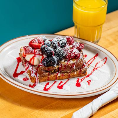 French toast topped with berries and icing drizzle, served with orange juice.