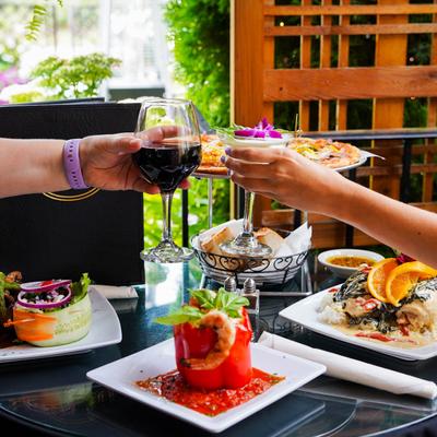 Two people toasting with drinks over a table with served dishes.