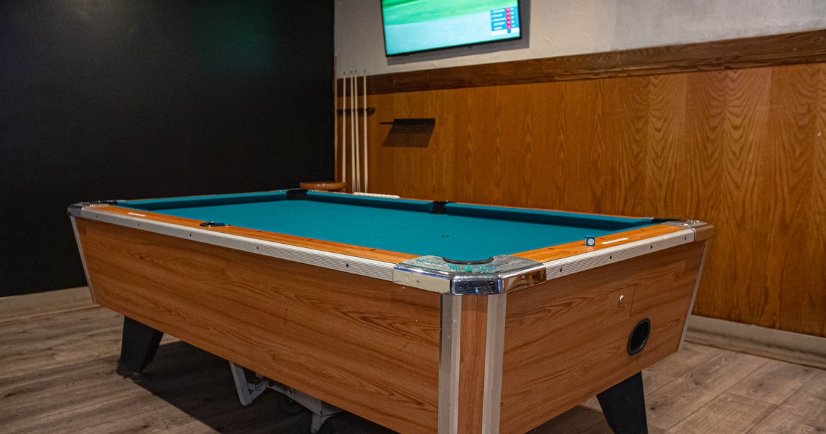 Pool table in a room with wooden walls and a TV screen above.