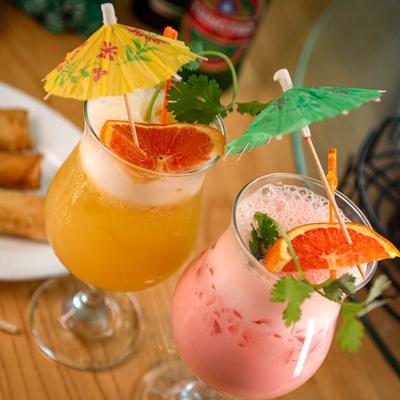 Pink and yellow drinks garnished with grapefruit slices, cilantro, and umbrellas.