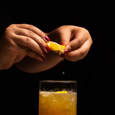 Hands squeezing a lemon wedge over the glass with a cocktail.