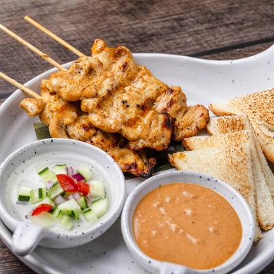 Grilled chicken skewers served with peanut sauce, fresh cucumber relish, and toast.