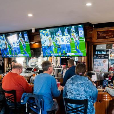 People saeting at the bar counter, watching sports on TV sceens.