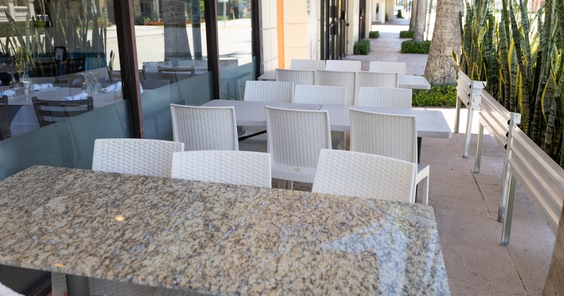 Exterior dining area of a restaurant with a granite table and white woven chairs