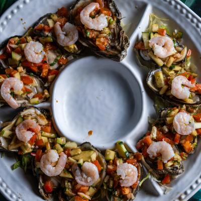 Platter featuring oysters on the half shell topped with diced vegetable and shrimp.