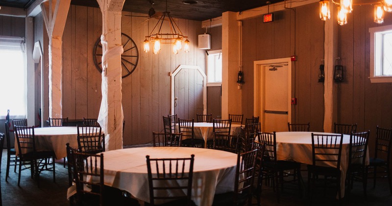 Interior, rustic dining room with round tables for six covered with white table cloths