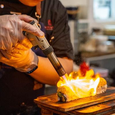 Sushi chef torching a roll on a wooden platform.