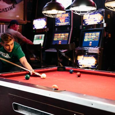 Interior, a guest playing pool, arcade game machines in the back