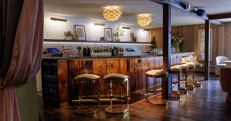 A rustic bar with golden stools and bottles of liquor displayed on shelves