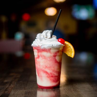 Miami Vice cocktail with whipped cream, cherry, and orange slice.