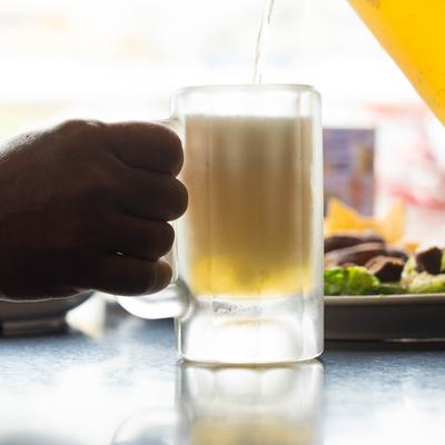 A person holding a pint glass of beer at a table, hand shot.