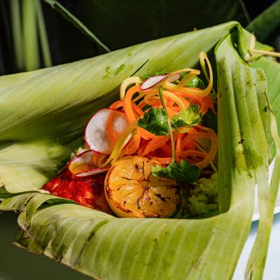 Grilled fish served in a banana leaf with vegetables and charred lemon half.