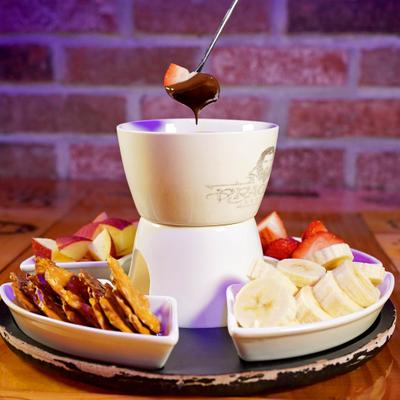 Chocolate fondue set with pretzels, sliced bananas, strawberries, and apples.