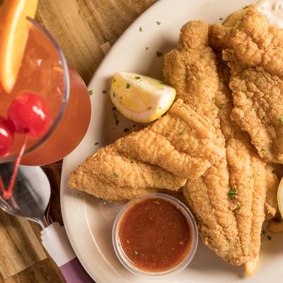 Fried catfish with Cajun fries and a red sauce for dipping, accompanied with a red cocktail.