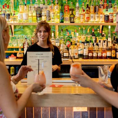 A smiling bartender conversing with two guests with frothy cocktails at the bar.