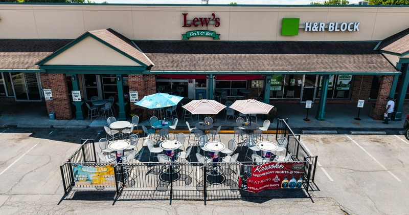 Exterior, aerial view to restaurant, parking lot and fenced off patio, tables, chairs, parasols, sign above entrance
