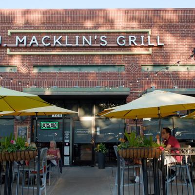 Storefront with signage, a brick facade, outdoor seating, and string lights.