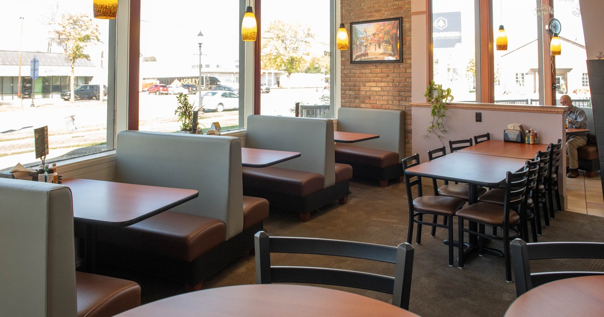 Interior of a restaurant with booths, tables, and decorative lights near large windows