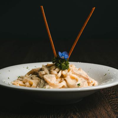 Fettuccine Alfredo with chicken, garnished with fresh parsley and tin breadsticks.