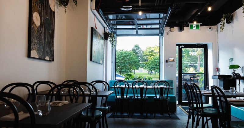 Interior of a restaurant with dark wood tables, bistro-style chairs, teal bench, abstract art