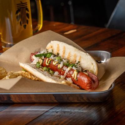 Hot dog topped with diced greed onions and mustard, served with chips.