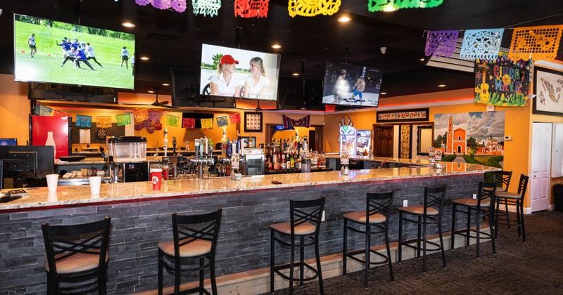 Interior of a bar with a marble topped counter, colorful paper banners, and mounted televisions
