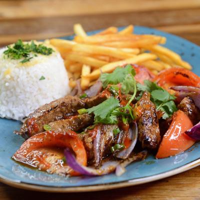 Steak strips with vegetables and rice and fries on a blue plate.