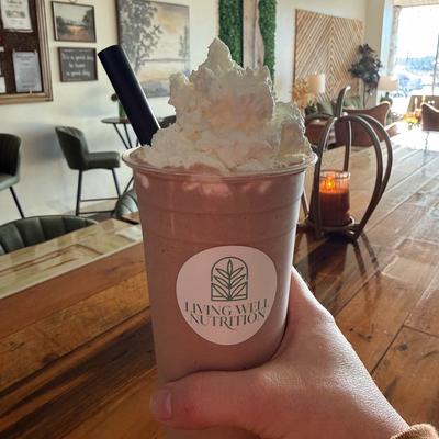 Hand holding a cup chocolate colored shake topped  with whipped cream.