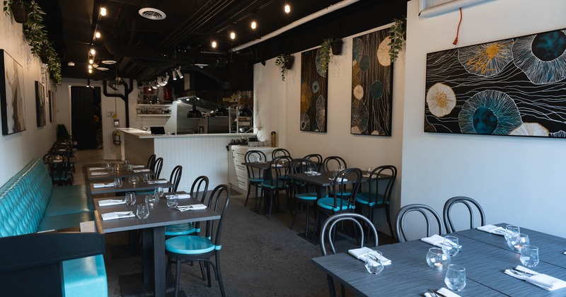 Interior of a modern restaurant with turquoise accents, abstract wall art, and an open kitchen