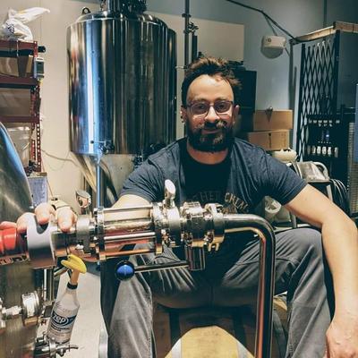 A person surrounded by large stainless steel brewing equipment.