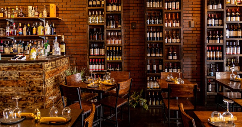 Rustic interior - brick walls and shelves with wine bottles, a wooden bar and set dining tables.