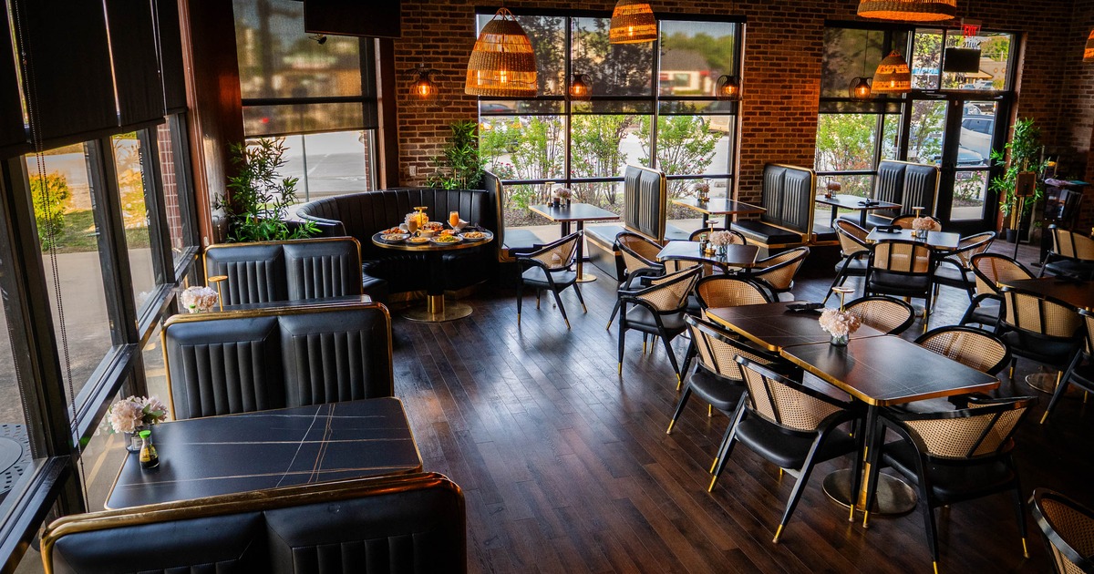 Interior of a modern restaurant with black seating, exposed brick walls, large windows, and pendant lighting