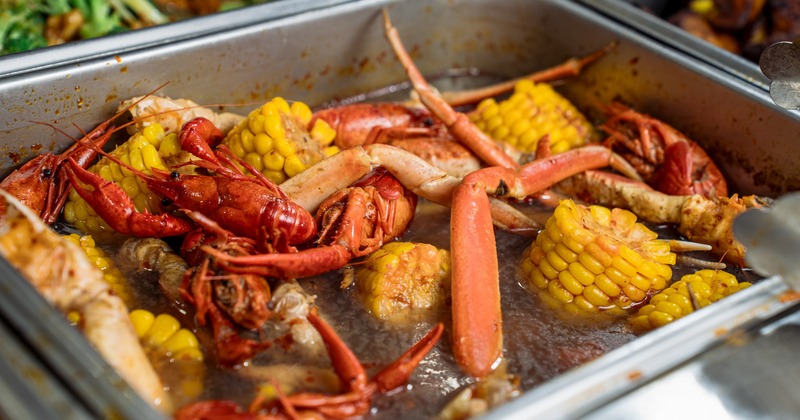 A metal buffet pan filled with crawfish, crab legs, and corn