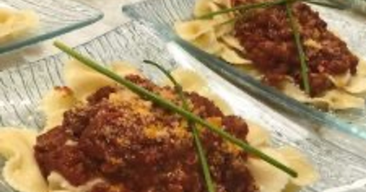 Bow-tie pasta topped with a thick meat sauce and a long green chive