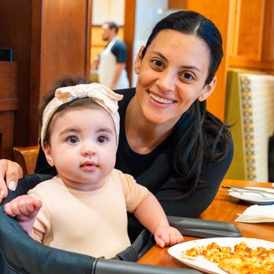 A smiling customer with a baby sits at a wooden table in dining area.