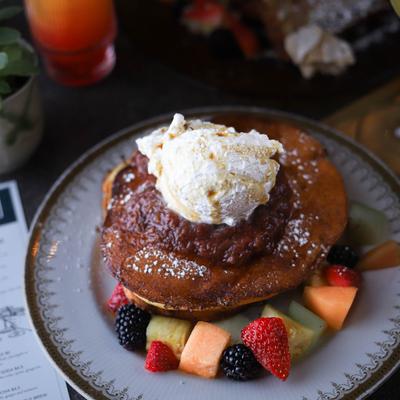 Pancakes topped with jam, vanilla whipped cream, and fruit.