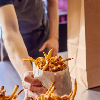 An employee placing paper bags filled with french fries on a counter.