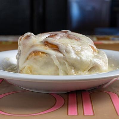 Cinnamon Roll topped with creamy icing, served on a white plate.
