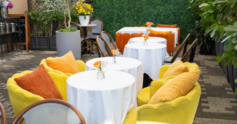 Outdoor café with white tablecloths and yellow-cushioned chairs, accented with orange flowers