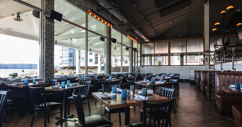 Interior of a modern restaurant with wooden tables, blue glasses, and floor-to-ceiling windows offering an outside view