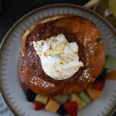 An overhead view of pancakes topped with jam, vanilla whipped cream, and fruit.