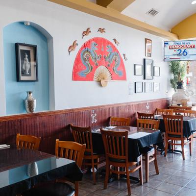 Thai restaurant interior with glass-top tables, wooden chairs, and wall decor.
